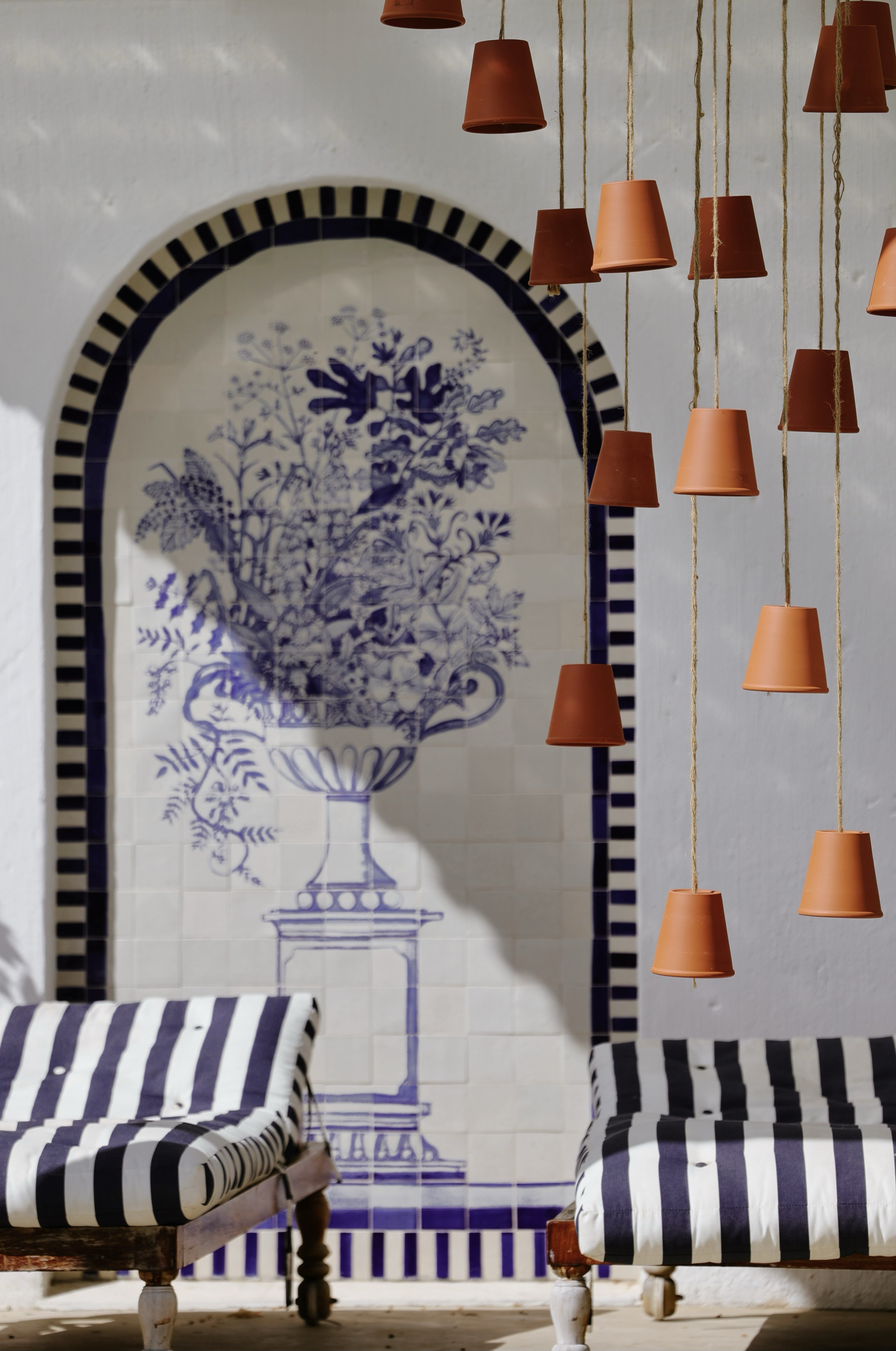Whitewashed courtyard with a blue and white tiled arch, hanging terracotta pots and striped daybeds