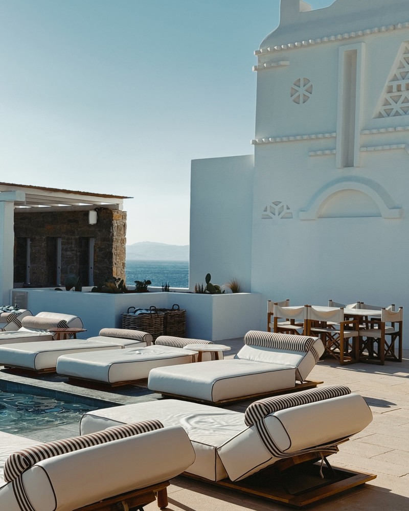 White daybeds with striped bolsters around a pool on a whitewashed Cycladic terrace