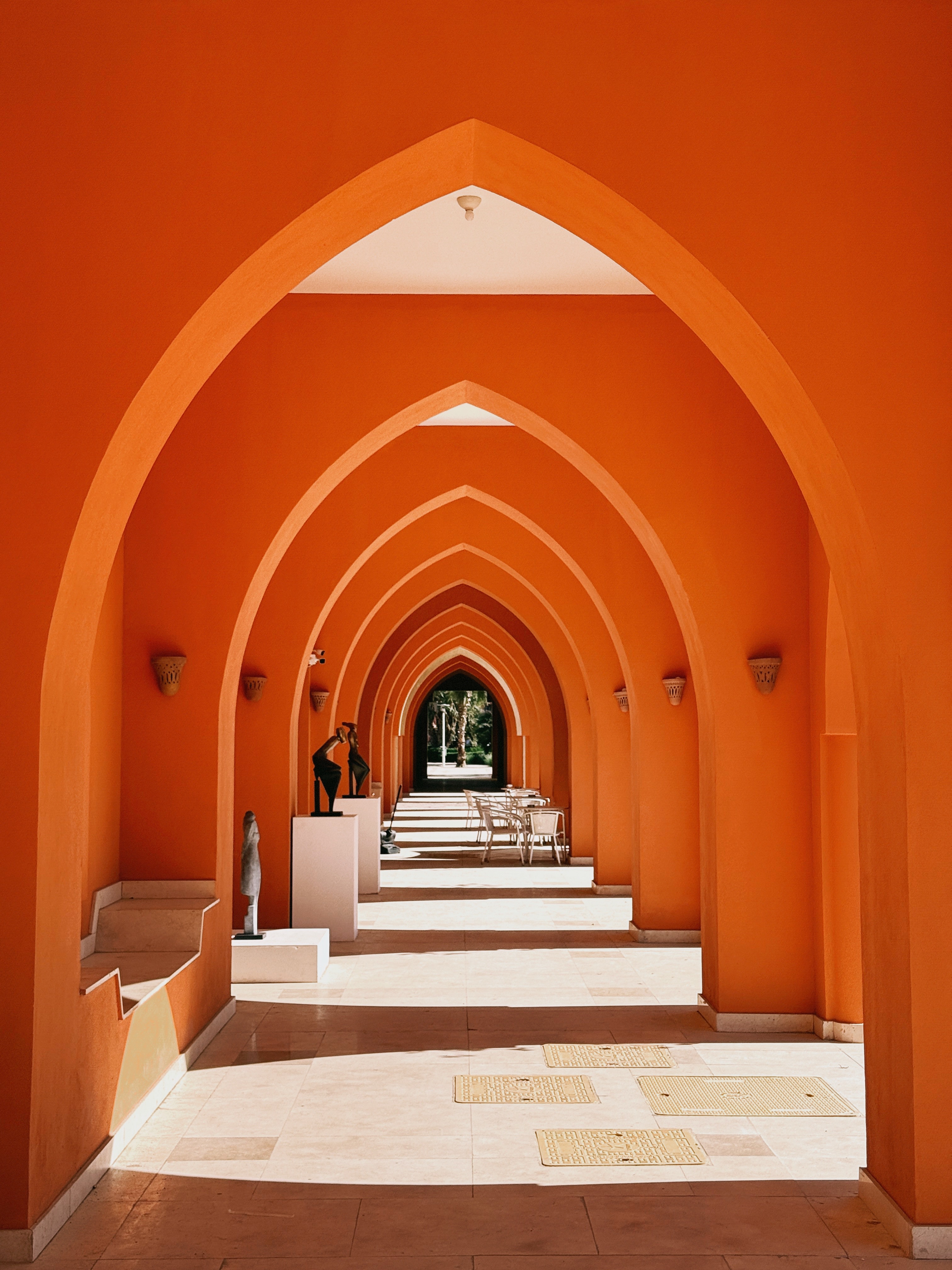 A colonnade of pointed orange arches lined with sculptures on white plinths
