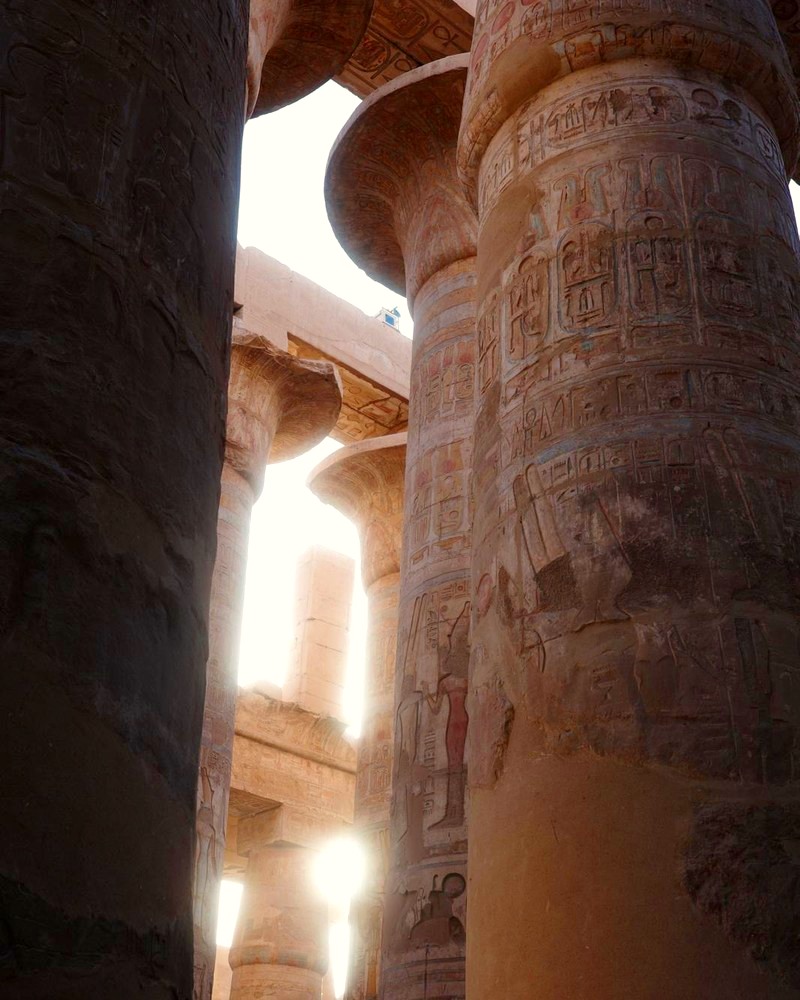 Towering carved temple columns with sunlight breaking through between them